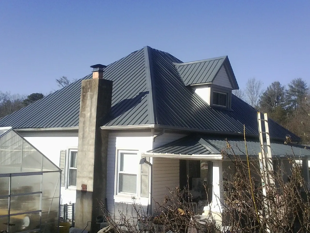 Dark blue standing seam metal roof on a white farmhouse with dormer — Slate & Tile Roof Repair by Roofing Brothers in Ludington