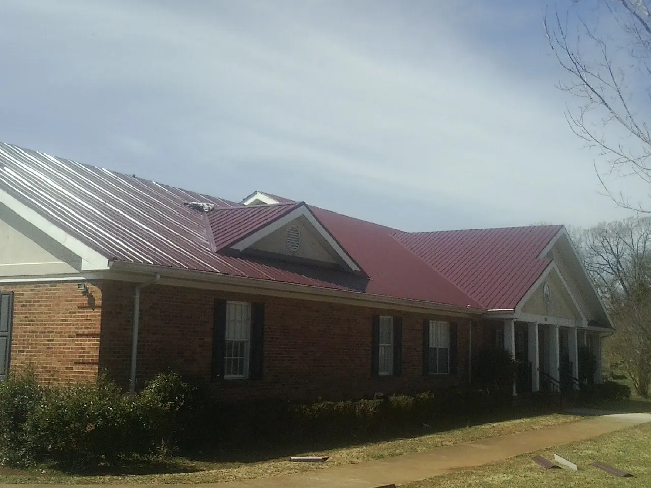 Red metal roof with gabled entries on a long brick building, from a Hail Damage Roof Repair job in Ludington