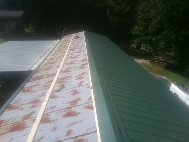 Old rusted panels beside newly installed green metal roofing — Wind Damage Roof Repair by Roofing Brothers in Ludington