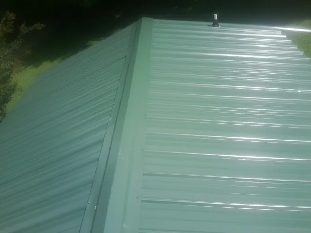 New green metal panels meeting at the ridge of a roof — Flat Roof Repair work by our crew in Ludington