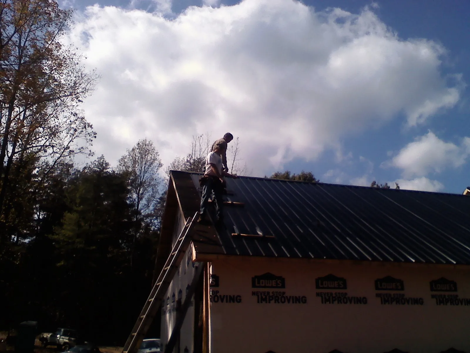 Roofer fastening dark metal panels high against a cloudy sky, from a Roof Inspection job in Ludington