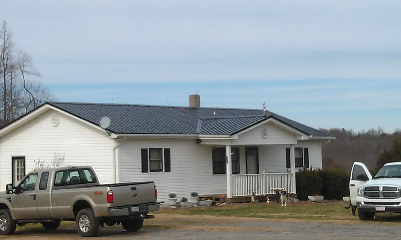Finished dark metal roof on a white ranch home with work trucks parked in Ludington