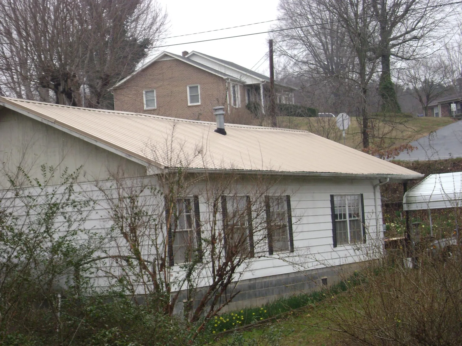 Tan metal roof on a white sided house set into a hillside — Commercial Roofing by Roofing Brothers in Ludington