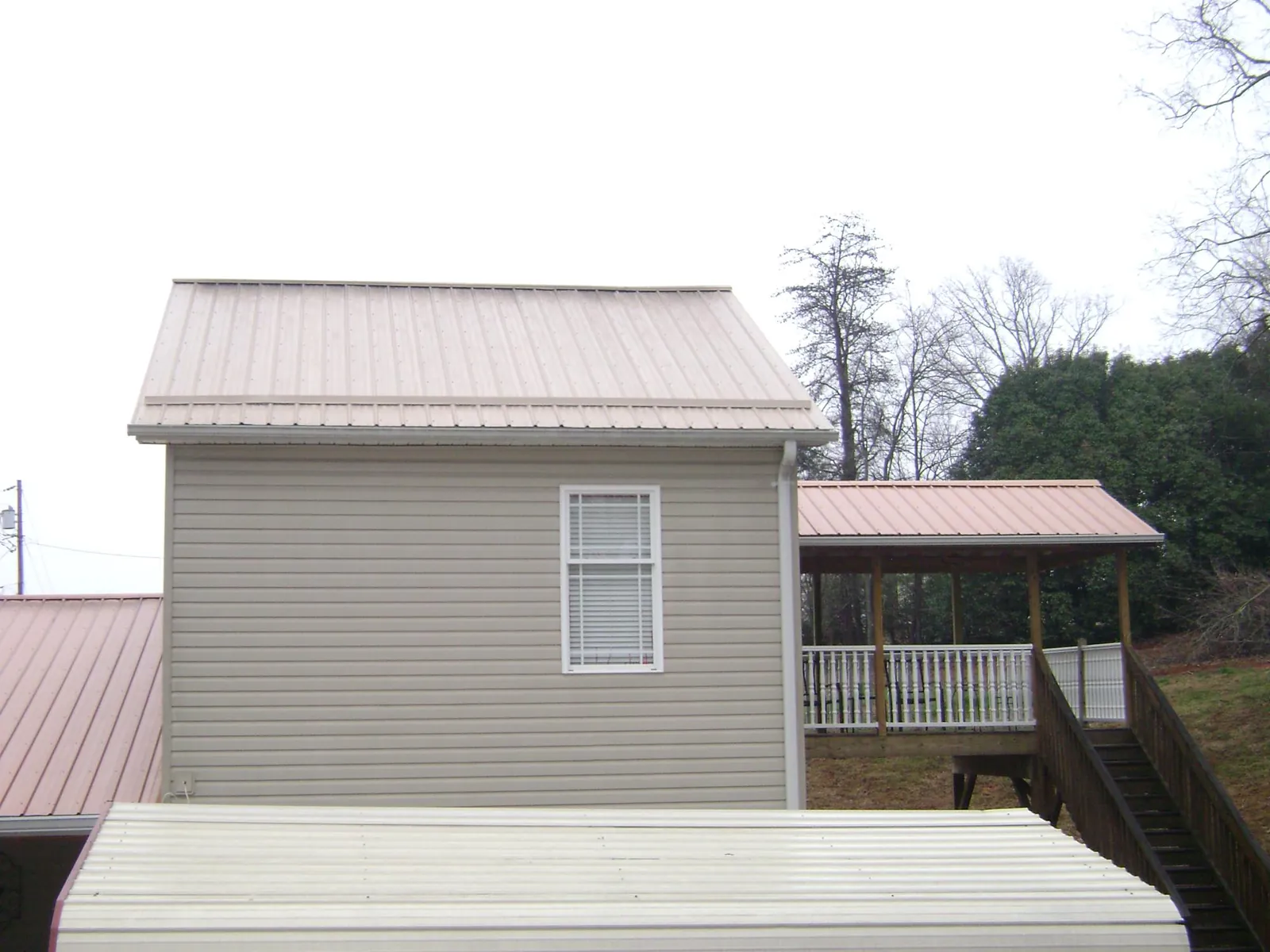 Tan metal roofs on a two story addition and attached porch, from a Roof Replacement job in Ludington
